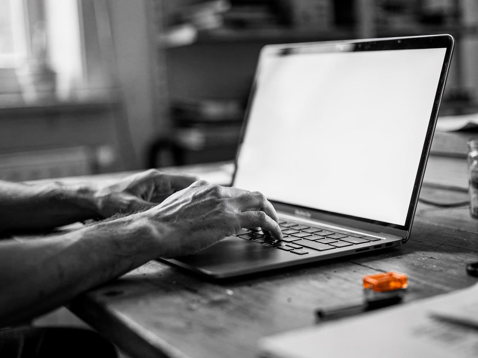 Handen typen op een laptop, in zwart-wit met één ember-accent