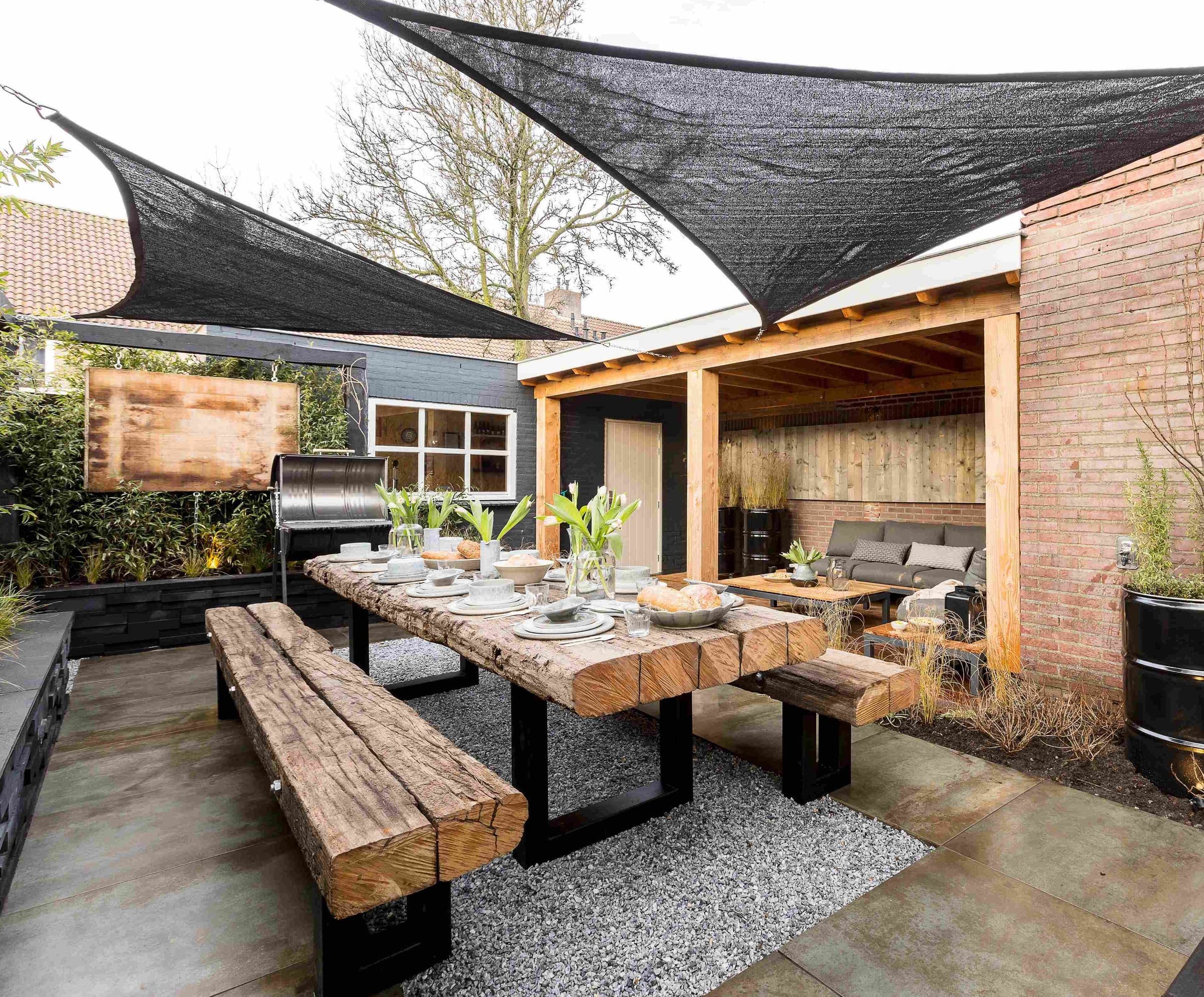 Terras met zwarte schaduwdoeken boven een houten eettafel